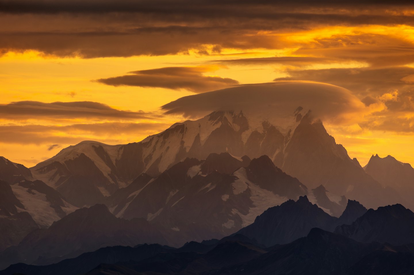 Schneebedeckte Berge mit einer Lentikularwolke bei Sonnenuntergang.