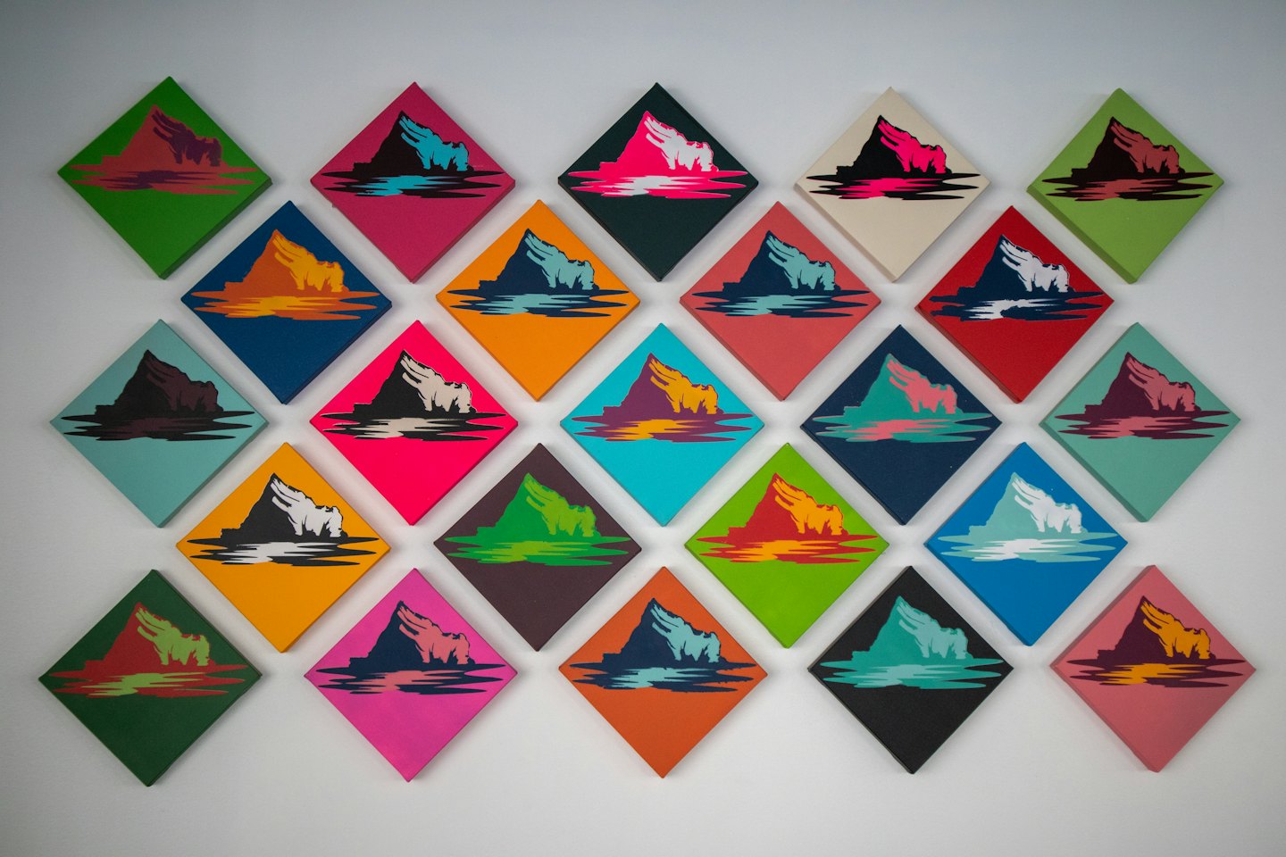 Fünfundzwanzig rautenförmige Berg-Kunstwerke hängen an einer weißen Wand.
