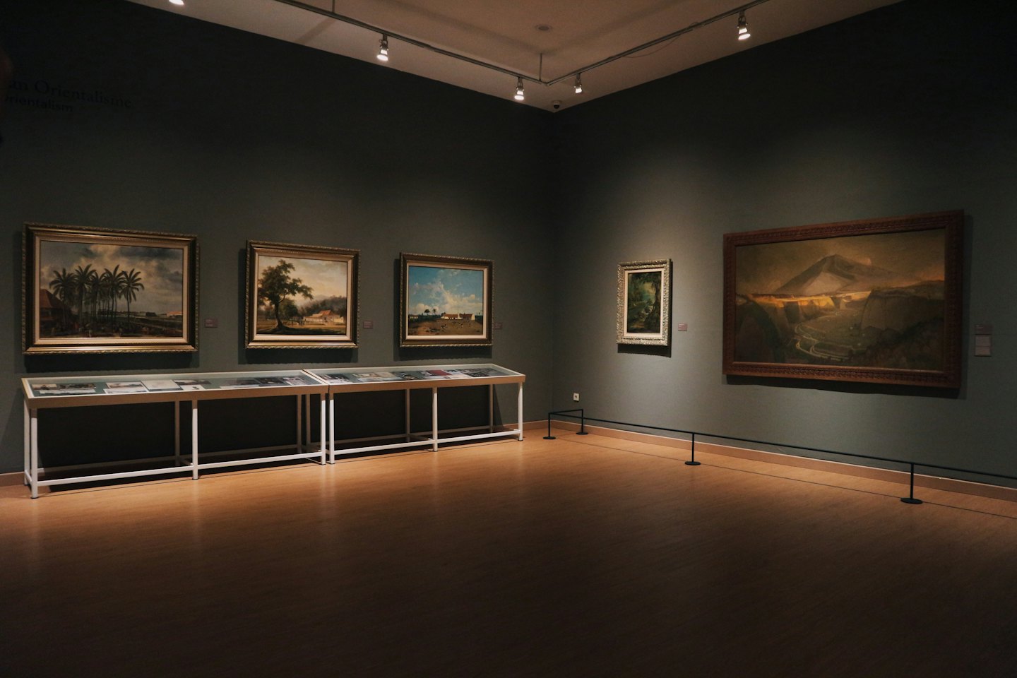 Leere Kunstgalerie mit Landschaftsgemälden an grauen Wänden.