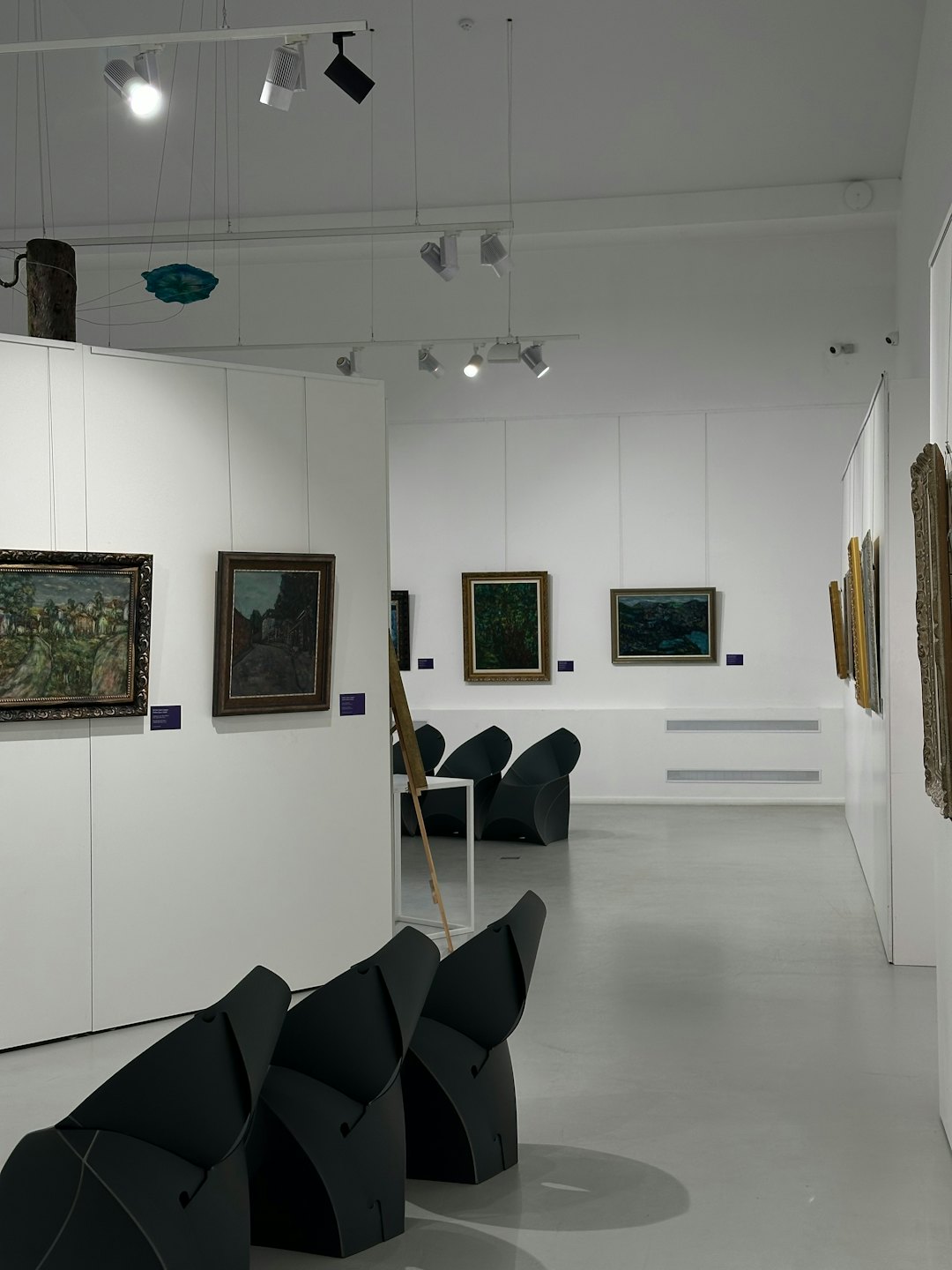 Moderne Kunstgalerie mit Landschaftsgemälden und hängenden Skulpturen.