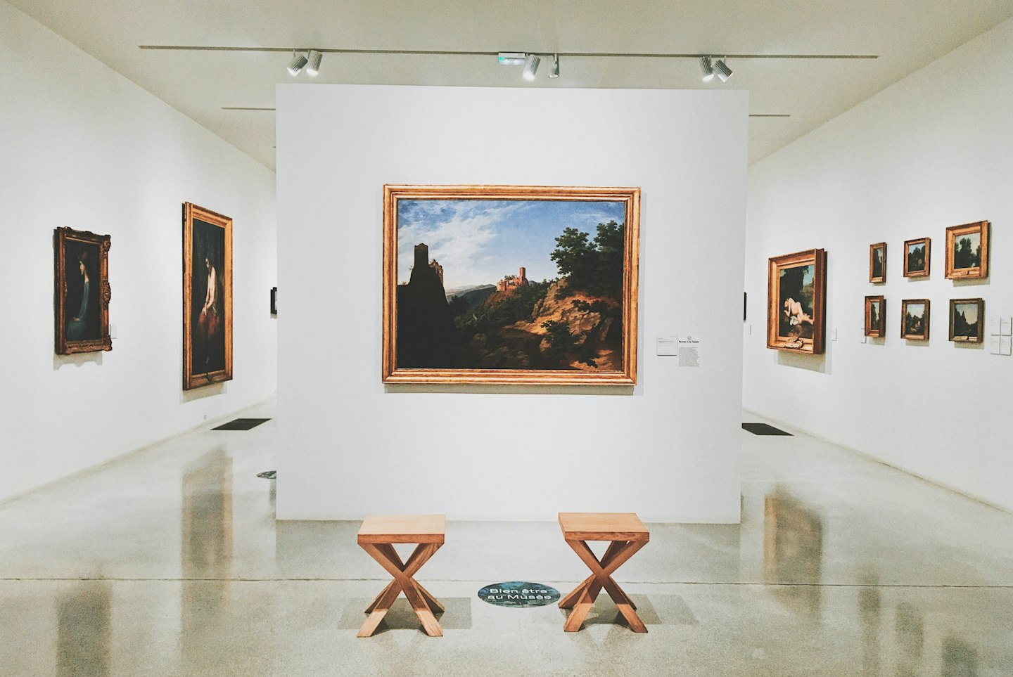 Gemälde hängen an weißen Galerie Wänden neben zwei Holzhockern.